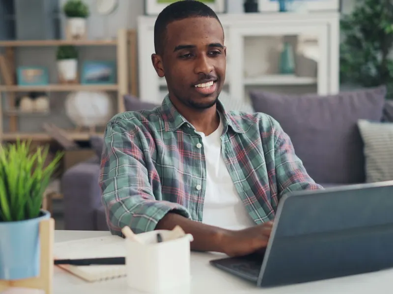 Pria tersenyum sambil menggunakan laptop di rumah