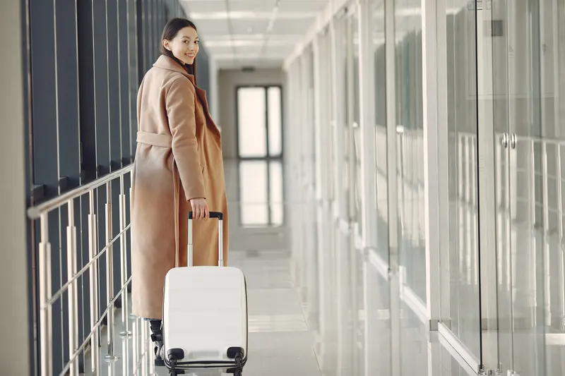 Femme souriante qui se retourne en tirant une valise dans un couloir d'aéroport